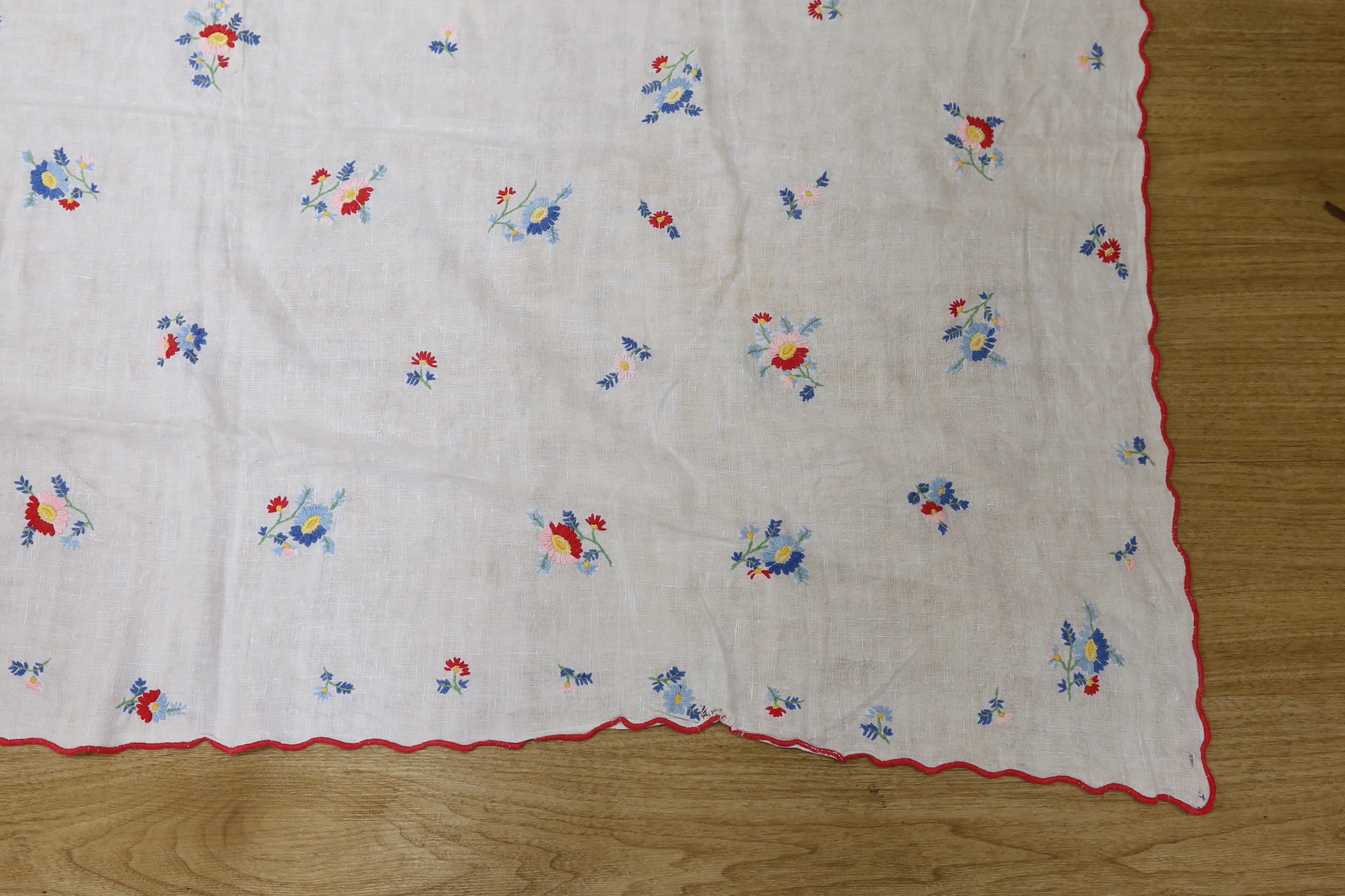 A 20th century woven linen panel, hand embroidered with scattered floral polychrome sprigs and a scalloped red buttonholed embroidered edge, possibly Swiss, 153 x 100cm